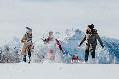 Winter im Salzburger Land: Familie macht eine Winterwanderung mit einem Schlitten. Bergpanorama im Hintergrund.