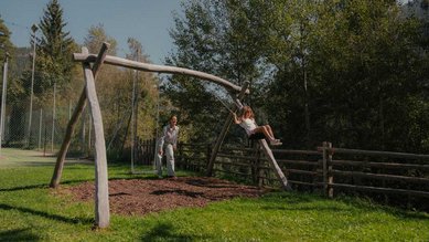 Mutter schaukelt gemeinsam mit ihrer Tochter draußen auf einer Wiese des Familienhotels Engel Gourmet & Spa