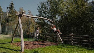 Mutter schaukelt gemeinsam mit ihrer Tochter draußen auf einer Wiese des Familienhotels Engel Gourmet & Spa