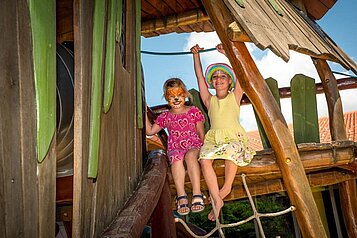 Zwei Kinder mit bunt bemalten Gesichtern spielen auf dem Outdoor-Spielplatz im Familienhotel Spa- & Familien-Resort Krone im Allgäu.