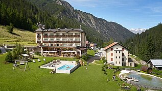 Außenansicht des Familienhotels Bella Vista in Südtirol im Sommer. Vor dem Hotel befinden sich ein Outdoor-Pool und Sonnenliegen.