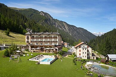 Außenansicht des Familienhotels Bella Vista in Südtirol im Sommer. Vor dem Hotel befinden sich ein Outdoor-Pool und Sonnenliegen.