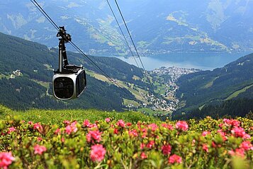 Blick von einem Berg auf eine Gondel und das Tal mit einem See 