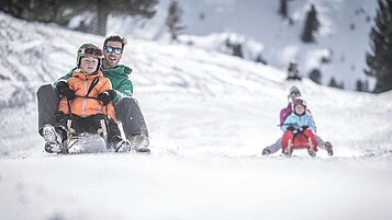 Familienhotel Alpenhof Dolomit Family im Winter. Familie hat beim gemeinsamen Rodeln Spaß.