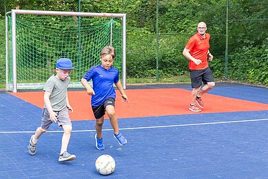 Zwei Jungs spielen mit ihrem Vater gemeinsam Fußball im Familienurlaub im Family Club Harz