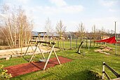 Großer Außenspielplatz mit Schaukeln und überdachten Sandkasten im Familienhotel Landhuus Laurenz im Münsterland.