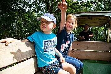 Zwei Kinder sitzen auf dem Anhänger eines Traktors und fahren eine Runde über das Hotelgelände des Landhuus Laurenz.