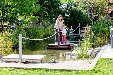 Eine Mutter mit ihrer Tochter auf einem Wasserspielplatz im Garten des Familienhotel Engel im Schwarzwald.