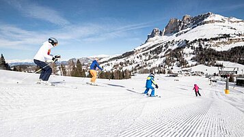 Kinder fahren die Skipiste mit einer Betreuerin in der Nähe vom Familienhotel Engel Gourmet & Spa in Südtirol runter.