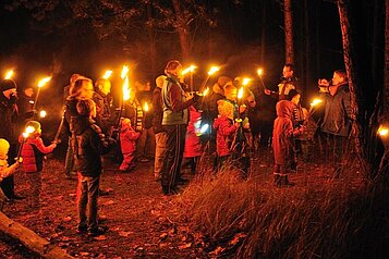 Viele Erwachsene und Kinder bei einer Fackelwanderung in der Dunkelheit im Familienhotel Borchard's Rookhus