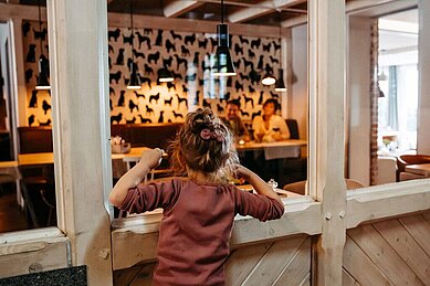 Vater und Mutter sitzen beim Abendessen gemeinsam am Tisch und haben die spielenden Kinder im Blick.