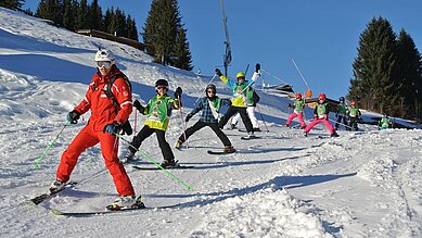 Kind mit Helm und Skiausrüstung steht auf verschneiter Piste vor einer malerischen Bergkulisse, was Wintersportaktivitäten für Kinder in einem familienfreundlichen Hotelumfeld veranschaulicht.