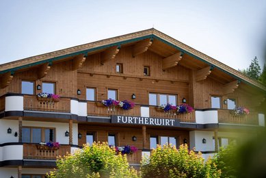 Außenansicht des Familienhotels Landgut Furtherwirt mit blumengeschmückten Balkonen und traditioneller Holzfassade.