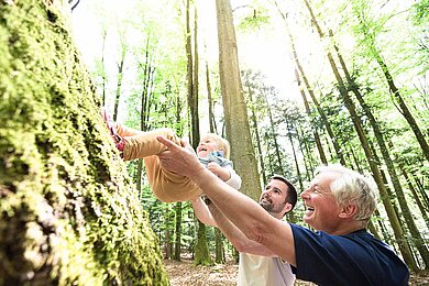 Ein Vater und Opa im Wald schwingen das Kind in die Luft