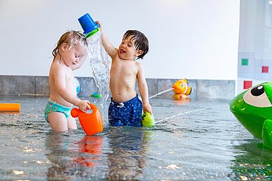 Zwei Kinder spielen im Kinderbecken und spritzen sich gegenseitig mit Wasser an im Familienhotel Familien Resort Petschnighof in Kärnten.