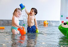 Zwei Kinder spielen im Kinderbecken und spritzen sich gegenseitig mit Wasser an im Familienhotel Familien Resort Petschnighof in Kärnten.