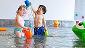 Zwei Kinder spielen im Kinderbecken und spritzen sich gegenseitig mit Wasser an im Familienhotel Familien Resort Petschnighof in Kärnten.