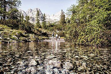 Familie beim Wandern in der schönen Natur der Tiroler Zugspitzarena. Im Hintergrund ist das Wettersteingebirge zu sehen. Die Familie wandert an einem klaren Bergsee.