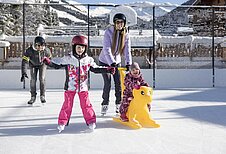 Kinder lernen das Eislaufen auf der Hoteleigenen Eislauffläche des Familienhotels Galtenberg in Tirol.