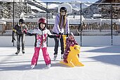 Kinder lernen das Eislaufen auf der Hoteleigenen Eislauffläche des Familienhotels Galtenberg in Tirol.