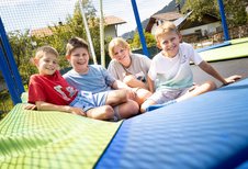 Vier Kinder sitzen fröhlich auf einem großen Trampolin im Familienhotel Krone im Allgäu.