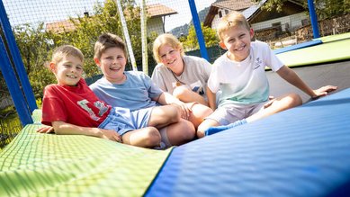 Vier Kinder sitzen fröhlich auf einem großen Trampolin im Familienhotel Krone im Allgäu.