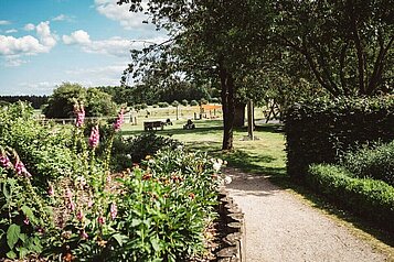 Großzügige Außenanlage des Familienhotels Landhaus Averbeck in der Lüneburger Heide mit blühenden Blumen und grünen Wiesen.