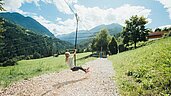 Mädchen sitzt auf einer Schaukel auf dem Outdoor-Spielplatz des Familienhotels Sailer. Der Spielplatz ist umgeben von Natur.