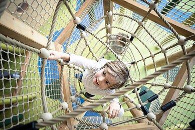 Junge klettert im Kletternetz auf dem Indoor Spielbereich des Allgäuer Berghofs.