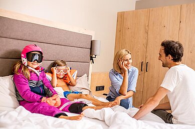 Kinder posieren auf Hotelbett im Skianzug und Badebekleidung für das Angebot vom Familienhotel Das Bayrischzell