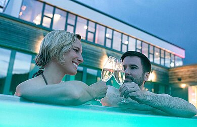 Eltern trinken im Pool des Familienhotels ein Glas Prosecco und geniessen die Aussicht im Outdoor-Pool