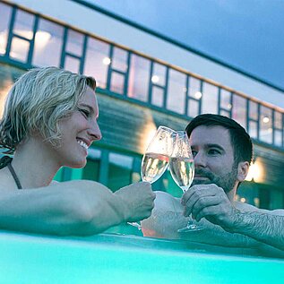 Eltern trinken im Pool des Familienhotels ein Glas Prosecco und geniessen die Aussicht im Outdoor-Pool