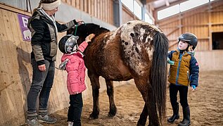 Kinder putzen mit der Reitlehrerin das Pony, in der Reithalle des Familotels Landhaus zur Ohe.