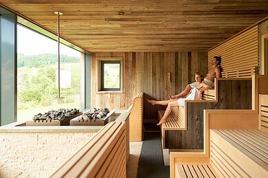 Entspanntes Paar in einer gemütlichen, mit Holz verkleideten Sauna im Familienhotel Schreinerhof im Bayrischen Wald.