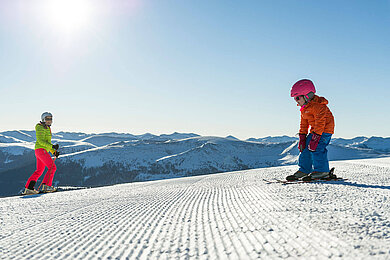 Familie in Kaernten im Winter beim Skifahren. Der Katschberg mit Sonne und blauem Himmel.