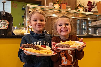 Zwei Kinder halten einen Teller mit Essen hoch und lachen.