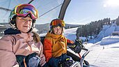 Kinder sitzen im Skilift des Familienhotels Elldus Resort im Erzgebirge.