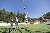 Kinder spielen auf dem Spielplatz des Familienhotels Galtenberg Family & Wellness Resort Basketball bei gutem Sommer Wetter.