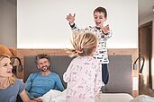 Vierköpfige Familie tobt auf dem Bett im Familienzimmer des Familienhotels Alpenhof Dolomit Family in Südtirol.