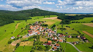 Luftaufnahme aus der Rhön. Zu sehen ist ein kleiner Ort, in dem das Familienhotel Rhön Feeling liegt und die umliegende Natur.