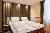 Gemütliches Hotelzimmer im Feldberger Hof mit einem Doppelbett, das ein kunstvolles, kronenförmiges Kopfteil besitzt, und holzvertäfelten Wänden für eine warme Atmosphäre.