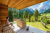 Eine junge Frau sitzt in der neuen Aussen-Sauna mit einem tollen Blick in die Berge im Familienhotel Bella Vista in Südtirol