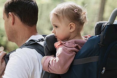 Vater wandert mit seinem Kleinkind in der Kraxe durch die Natur rund ums Familienhotel Tirolerhof