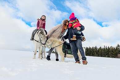 Eine Familie bei Ausritt mit Pferden in winterlicher Landschaft auf dem Hof vom Ulrichshof Nature · Family · Design geführt wird.