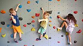 Drei Kinder klettern die Kletterwand in der Indoor-Spielhalle vom Familienhotel Das Bayrischzell in Oberbayern hoch.