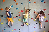 Drei Kinder klettern die Kletterwand in der Indoor-Spielhalle vom Familienhotel Das Bayrischzell in Oberbayern hoch.