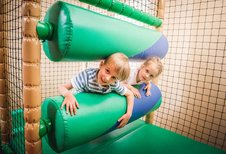 Zwei Kinder haben Spaß im Indoor-Spielbereich des Landguts Furtherwirt und klettern lachend durch weiche, grüne Hindernisse