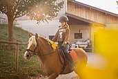 Ein Kind reitet auf einem Haflinger mit Blumen im Haar.