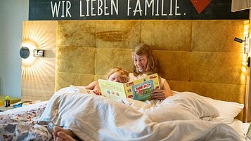 Mutter und Kind genießen die Zeit im Familienhotel Landhaus zur Ohe im Bayerischen Wald und liegen im großen Familienbett.