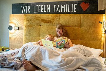 Mutter und Kind genießen die Zeit im Familienhotel Landhaus zur Ohe im Bayerischen Wald und liegen im großen Familienbett.